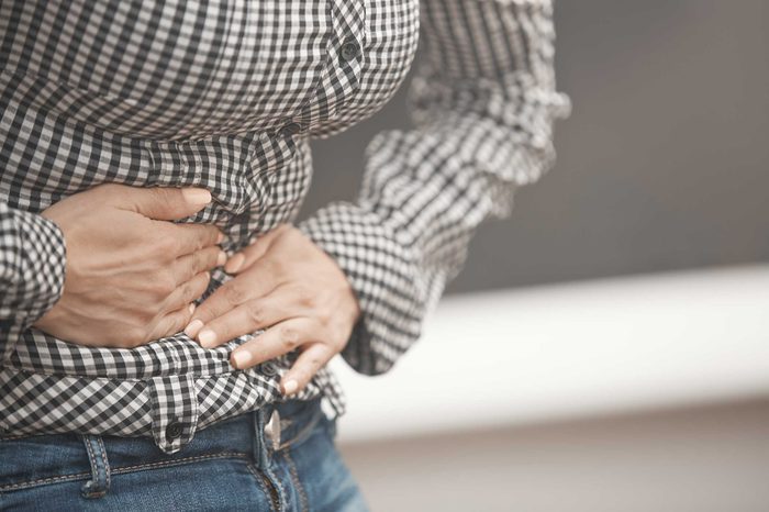 Woman wearing a plaid shirt hunched over clutching her stomach.
