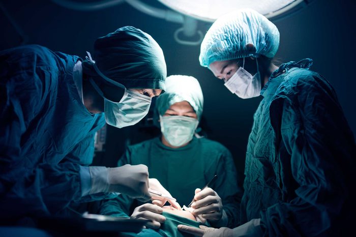 Group of surgeons and surgeon's assistants underneath a light, using operating tools.