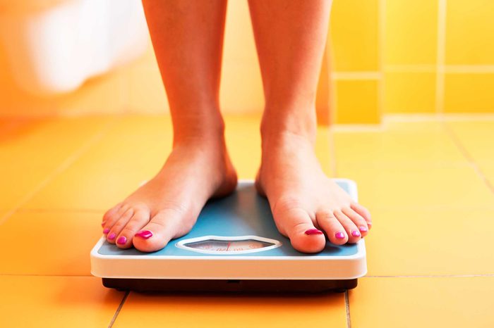 Woman's legs on top of a blue scale, weighing herself in a yellow bathroom.