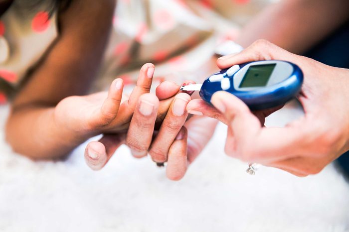 Woman helping a younger girl check her blood glucose levels with a glucose meter.