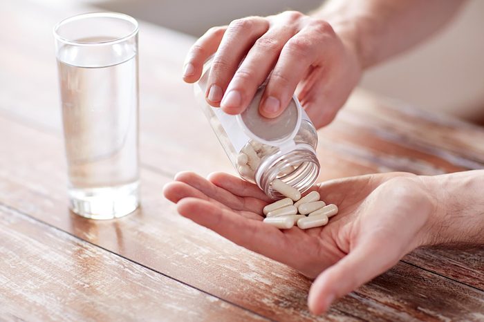 person shaking supplements into hand next to a glass of water on a table