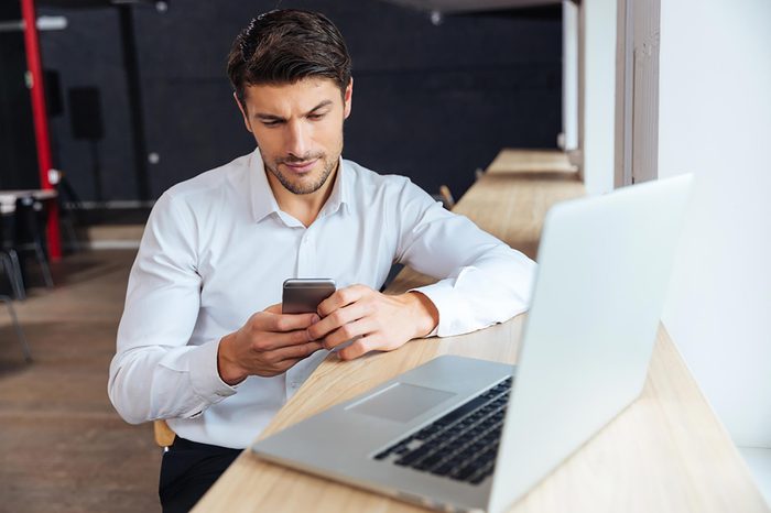 man checking his cellphone while at his computer