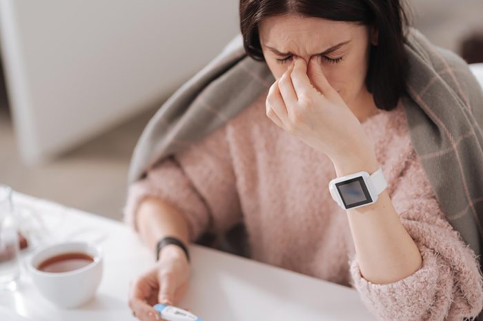 sick woman with a thermometer pinching the bridge of her nose and wincing