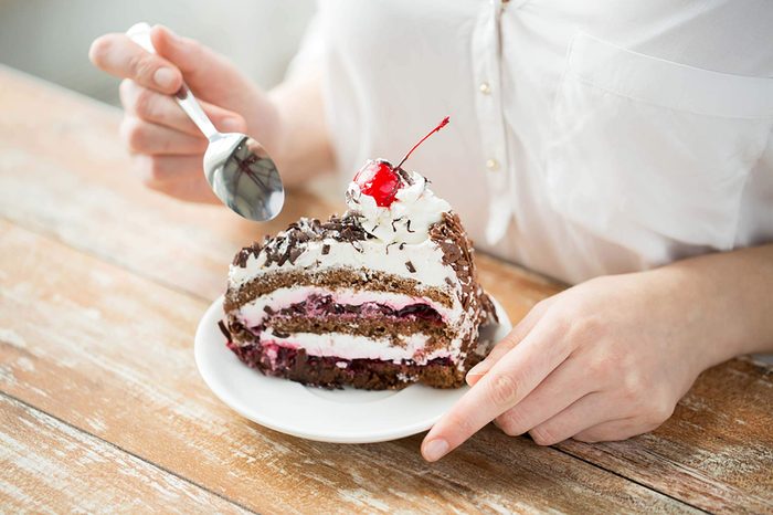 Person eating chocolate cream cake with cherry on top