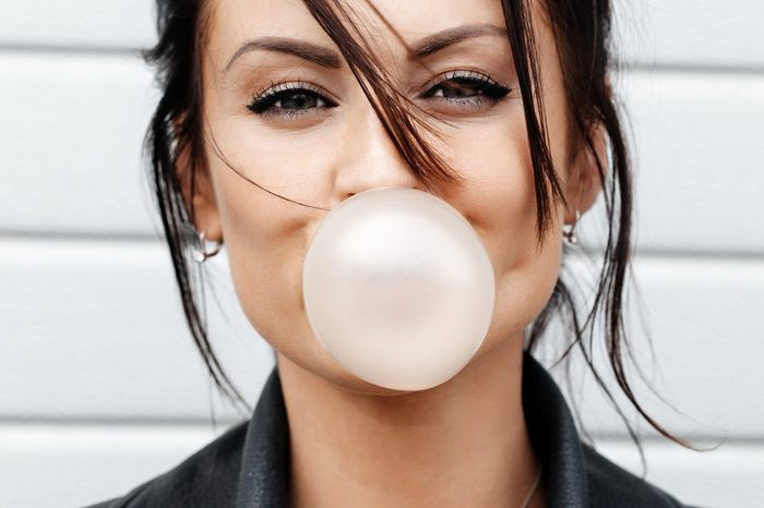 Outdoor lifestyle portrait of beautiful young woman blowing a bubble gum balloon