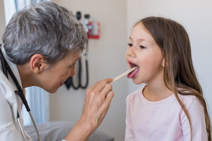 Doctor examining little girl's mouth and tonsils at the doctor's office.