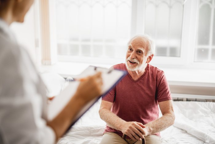 Portrait of bearded gentleman with walking stick discussing his state of health with female physician. He is looking at young lady with smile