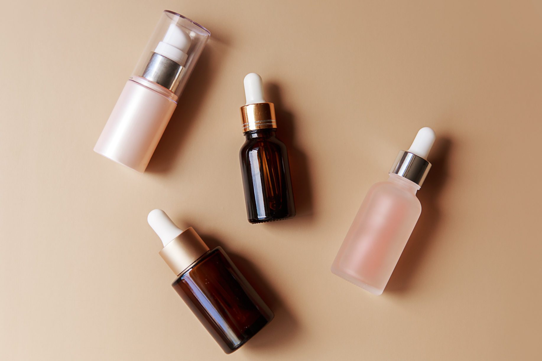 Set of amber glass cosmetic bottles on brown background. Pump bottle, dropper bottle, dispenser cosmetic container Flat lay, top view.