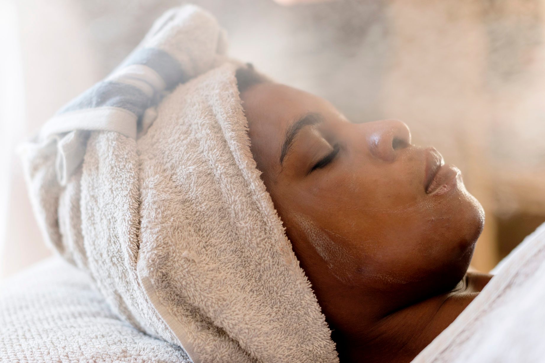 woman with towel on her hair receiving steam treatment at spa