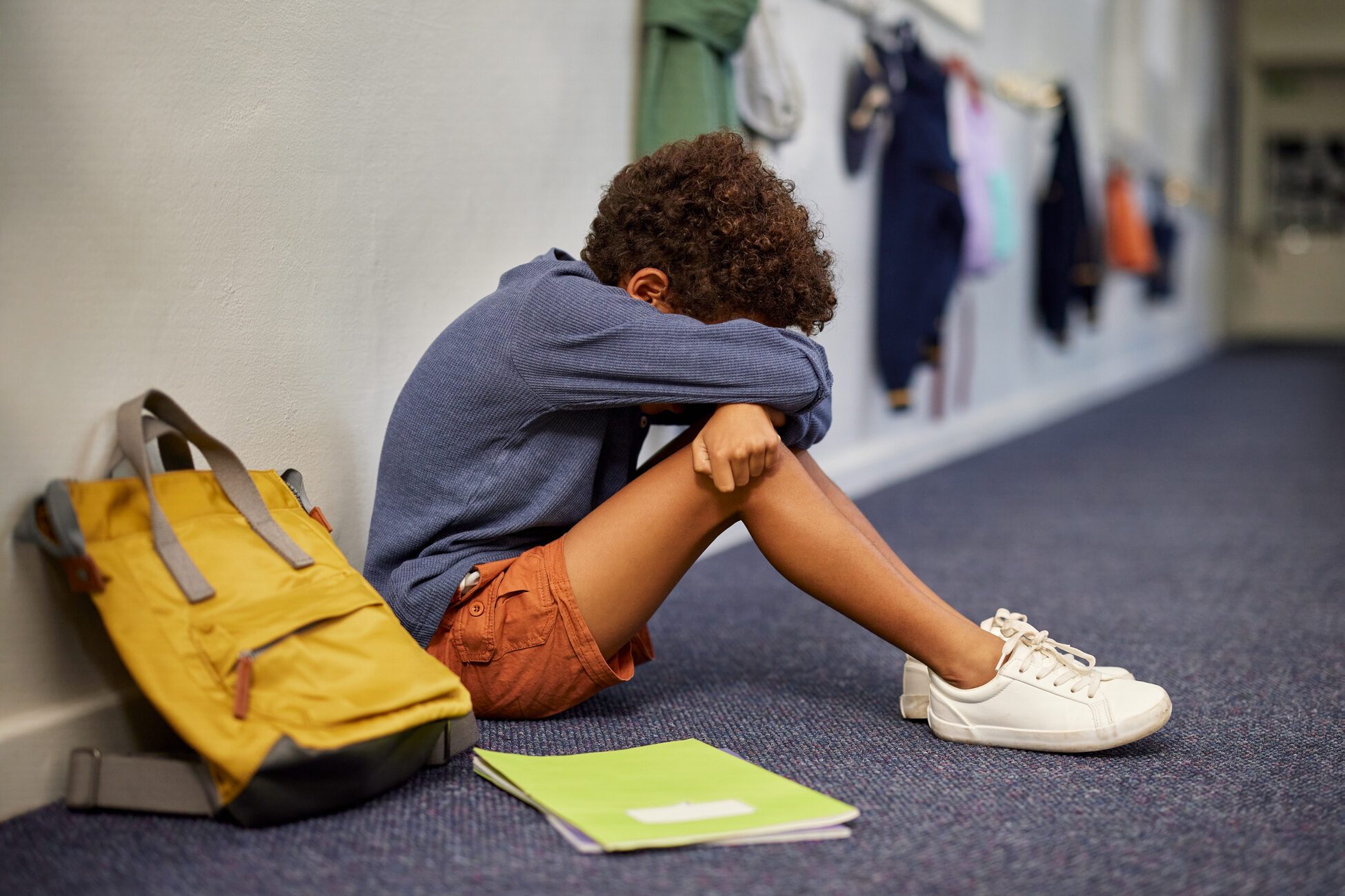 Depressed boy sitting on corridor floor at school