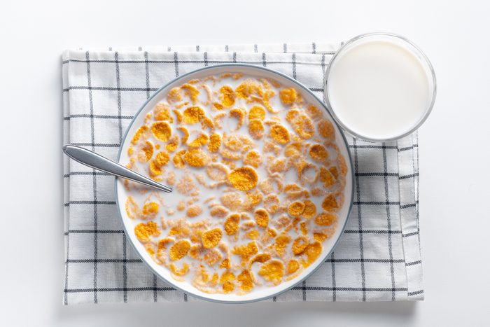 Dry honey cornflakes in a ceramic plate on the dining table at home or on a white background. Flakes with organic farm vegetable soy, almond or animal milk. Top view, copy space. The concept of healthy eating, vegetarian and vegan food for breakfast.